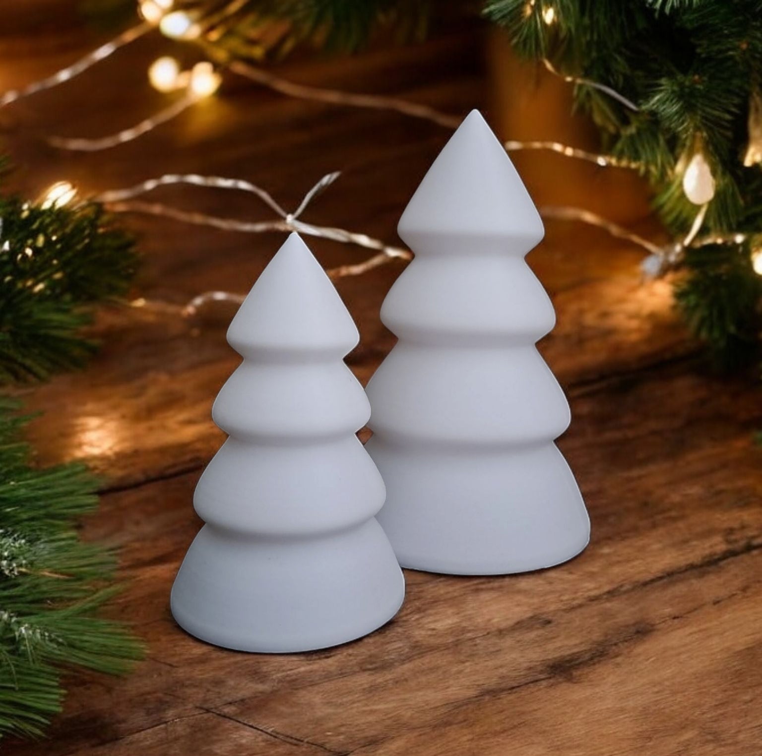 Two white Christmas tree-shaped lights on a wooden surface with festive background