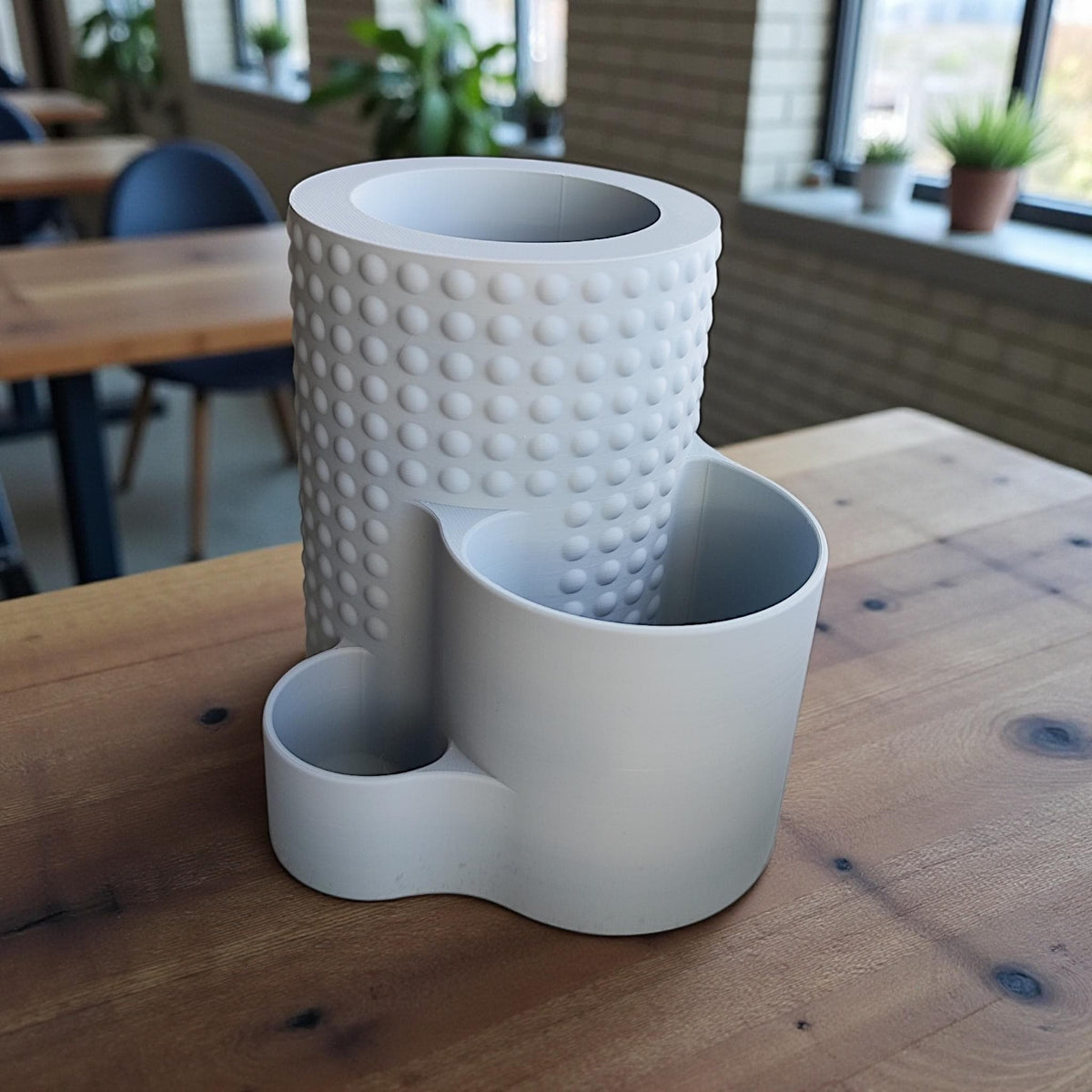 Empty tiered dimple pencil pot on a wooden table, showing its three compartments