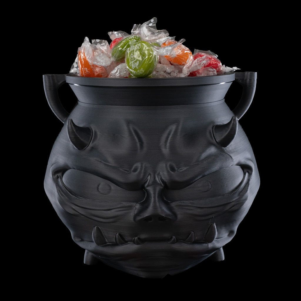 Black cat-shaped cauldron with Halloween-themed candy on a black background
