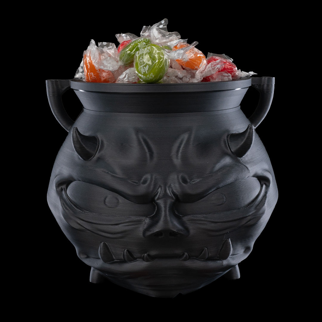 Black cat-shaped cauldron with Halloween-themed candy on a black background