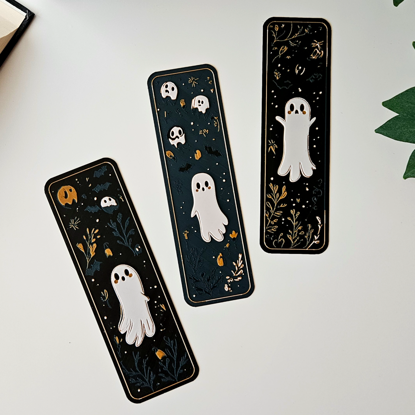 Three Halloween-themed bookmarks with ghosts and autumn leaves on a white surface.
