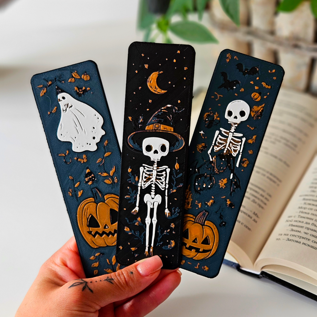 Three Halloween-themed bookmarks held by a hand with an open book in the background.