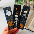 Three Halloween-themed bookmarks held by a hand with an open book in the background.