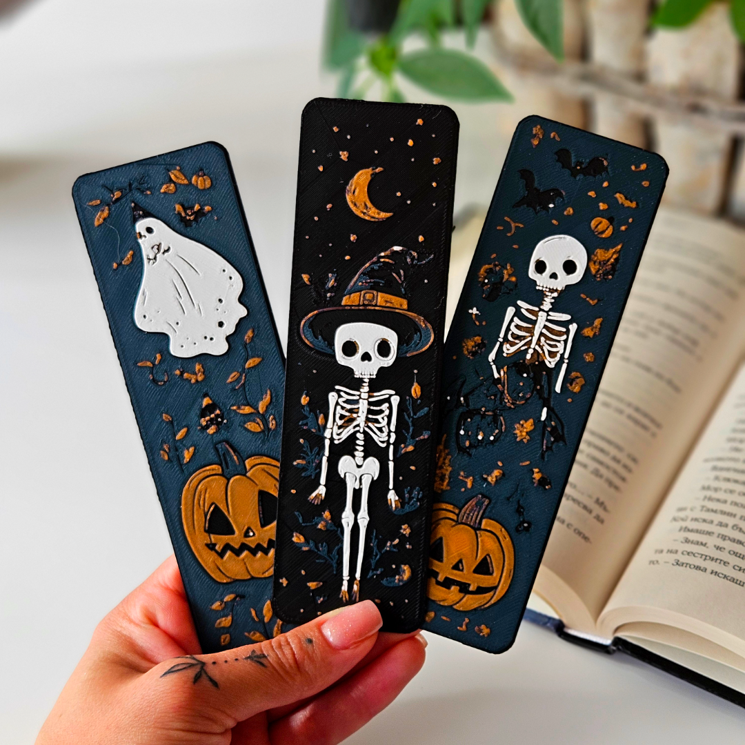Three Halloween-themed bookmarks held by a hand with an open book in the background.