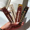 Decorative bookmarks with sword designs held by a hand against an open book.