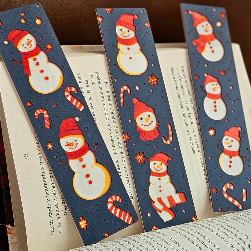 Three Christmas-themed bookmarks with snowmen and candy canes on a book background.