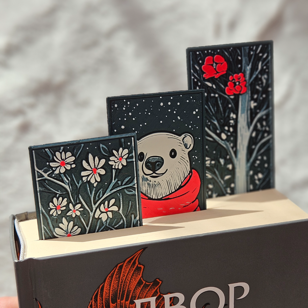 Three small books with illustrated covers featuring a bear, flowers, and a tree on top of a larger book.