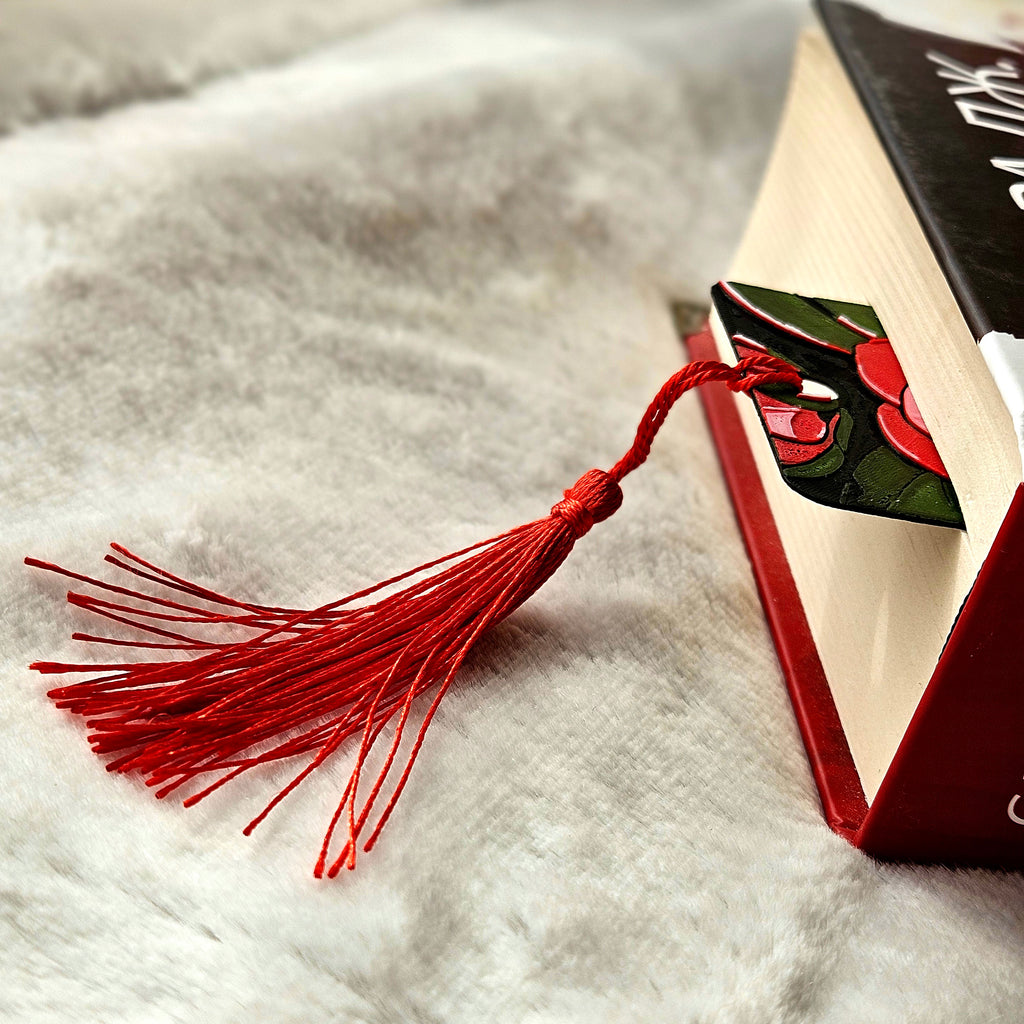 Red tassel bookmark on an open book with a decorative cover on a textured surface.