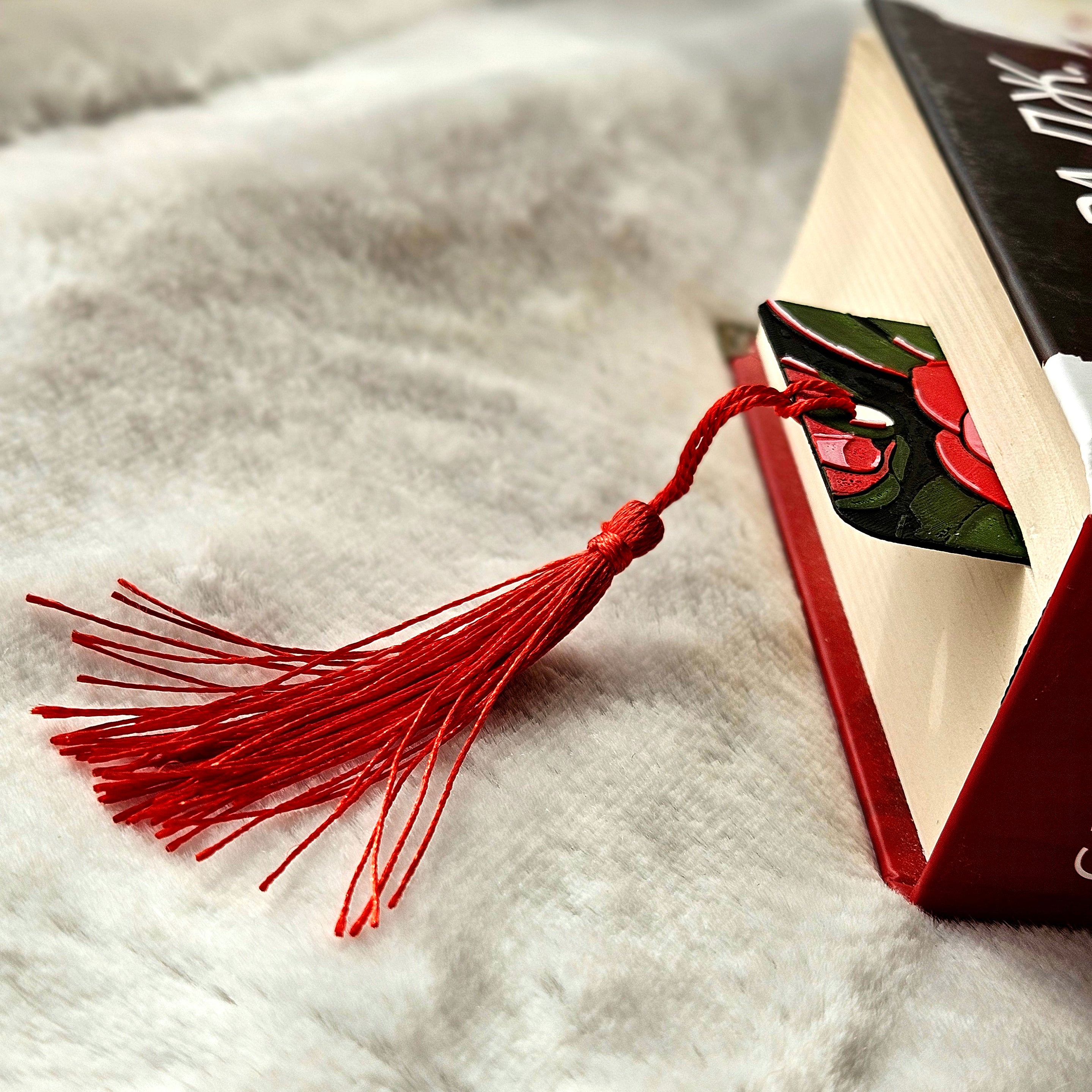 Red tassel bookmark on an open book with a decorative cover on a textured surface.