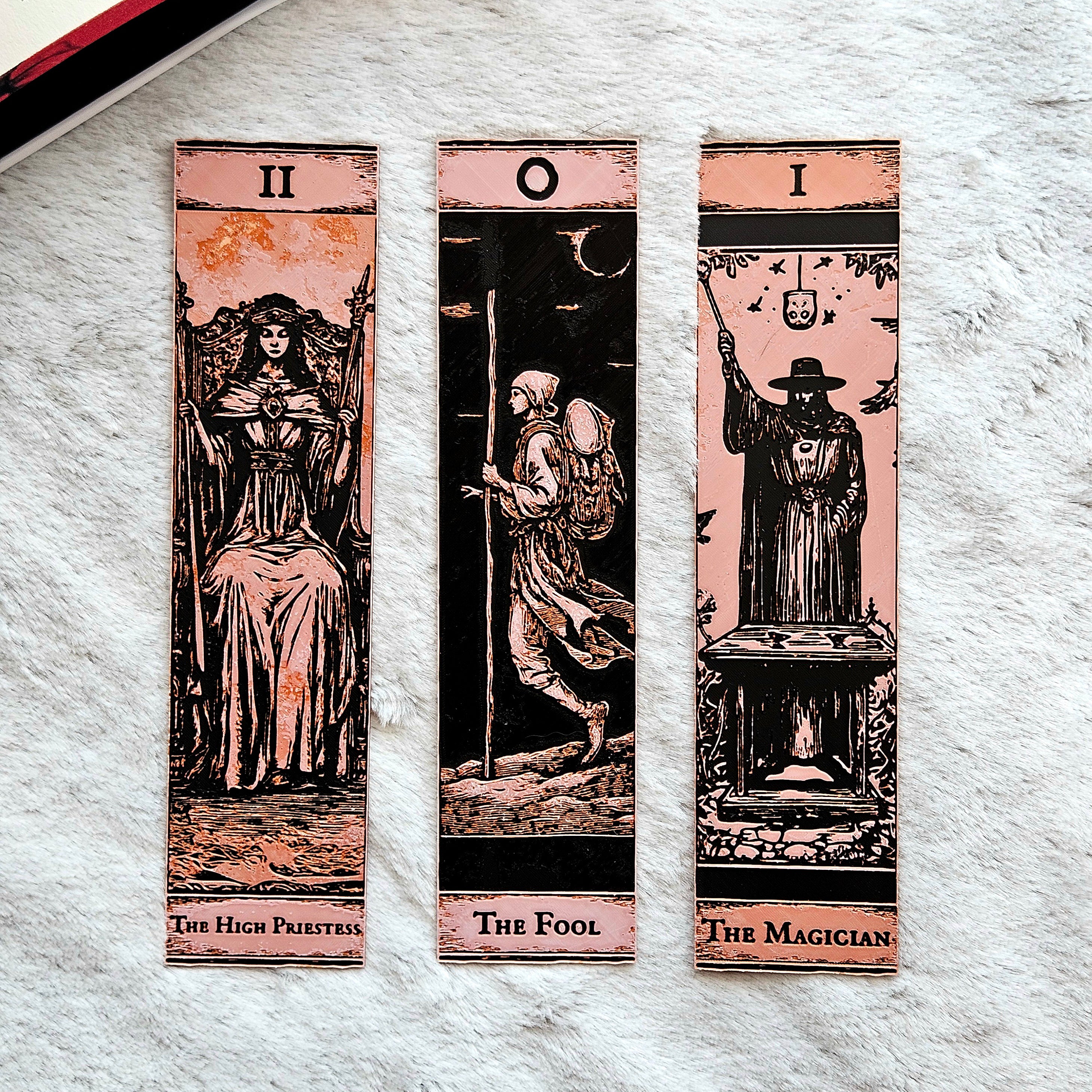 Three tarot card bookmarks titled 'The High Priestess', 'The Fool', and 'The Magician' on a textured surface.