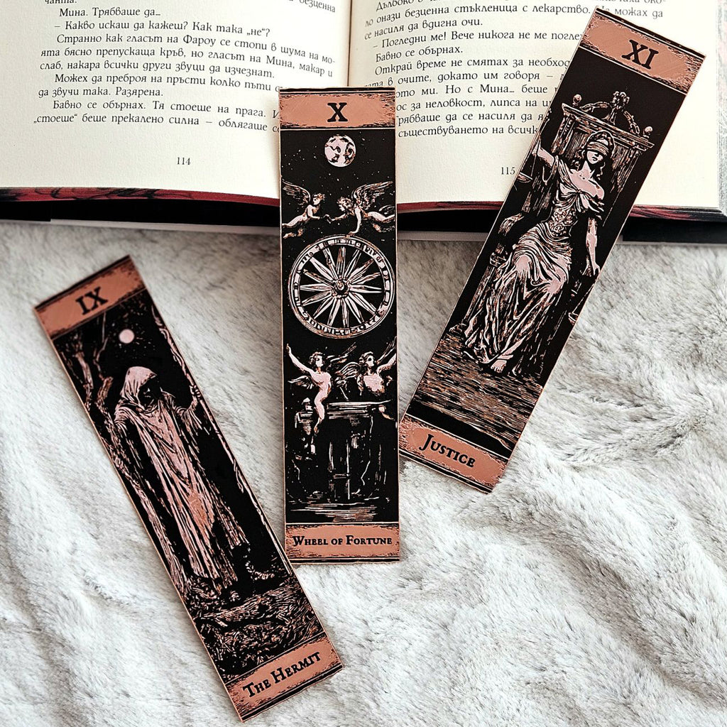 Three tarot card bookmarks on a textured surface with an open book in the background.