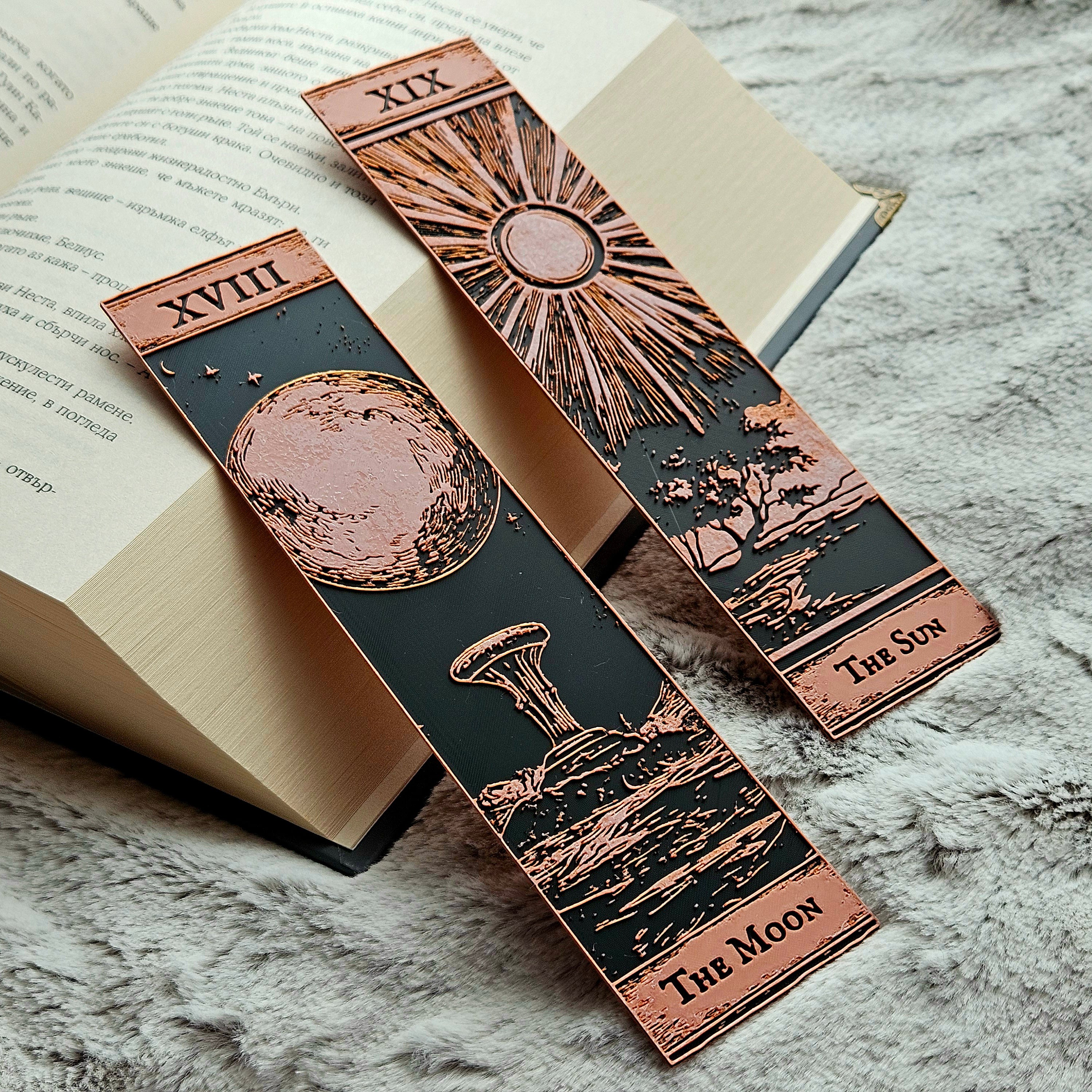 Three ornate bookmarks with celestial designs on an open book.