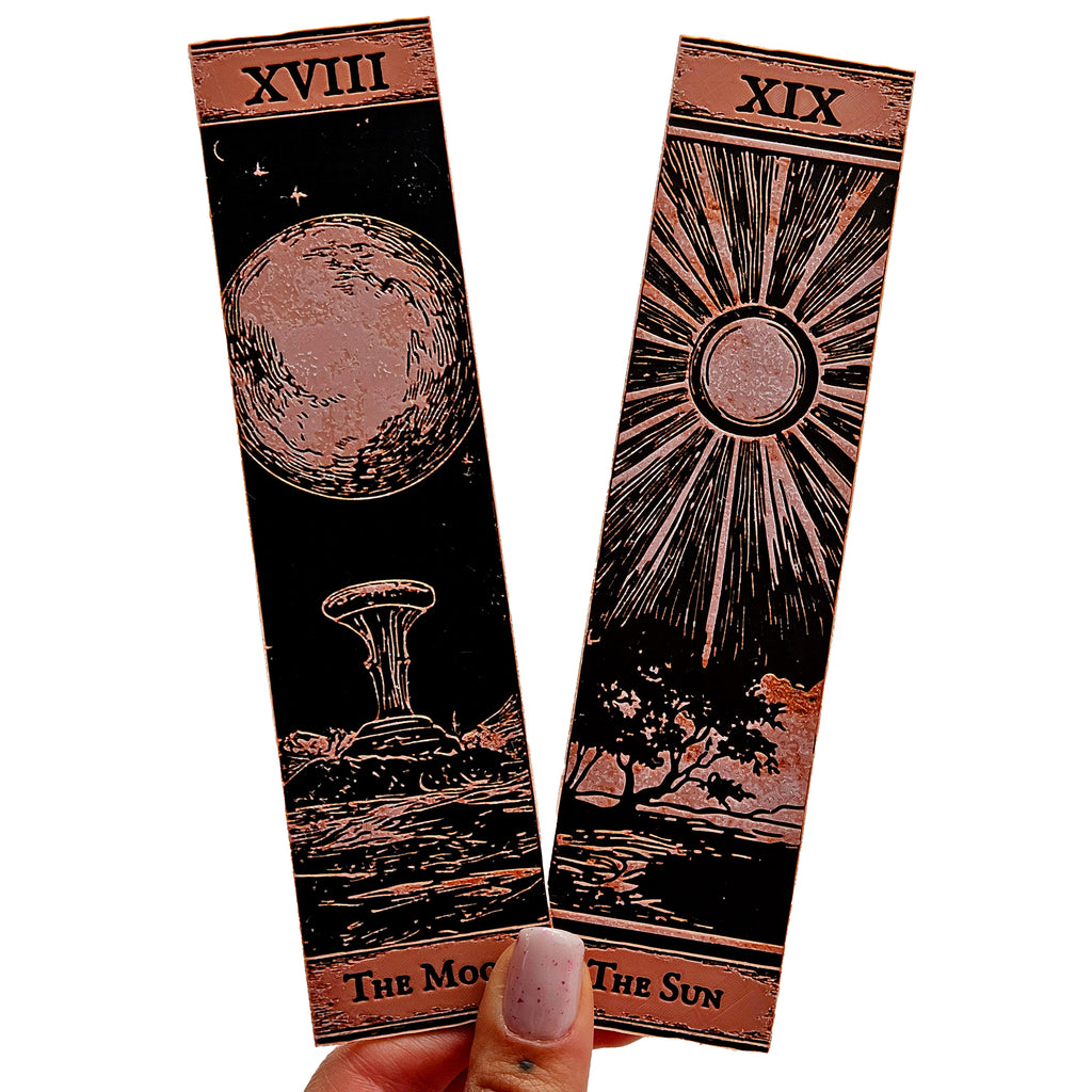 Two tarot card designs, 'The Moon' and 'The Sun', held by a hand on a white background.