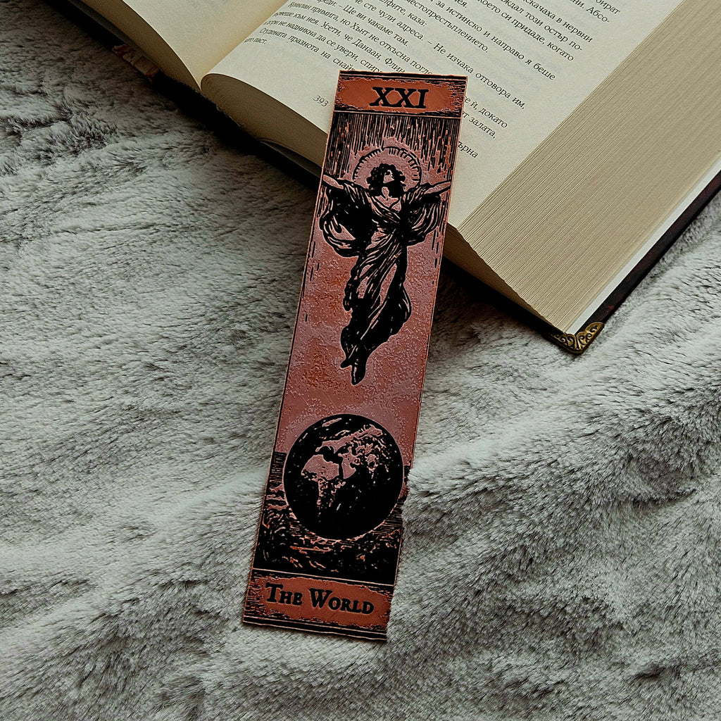 Decorative bookmark with tarot design on a textured surface next to an open book.