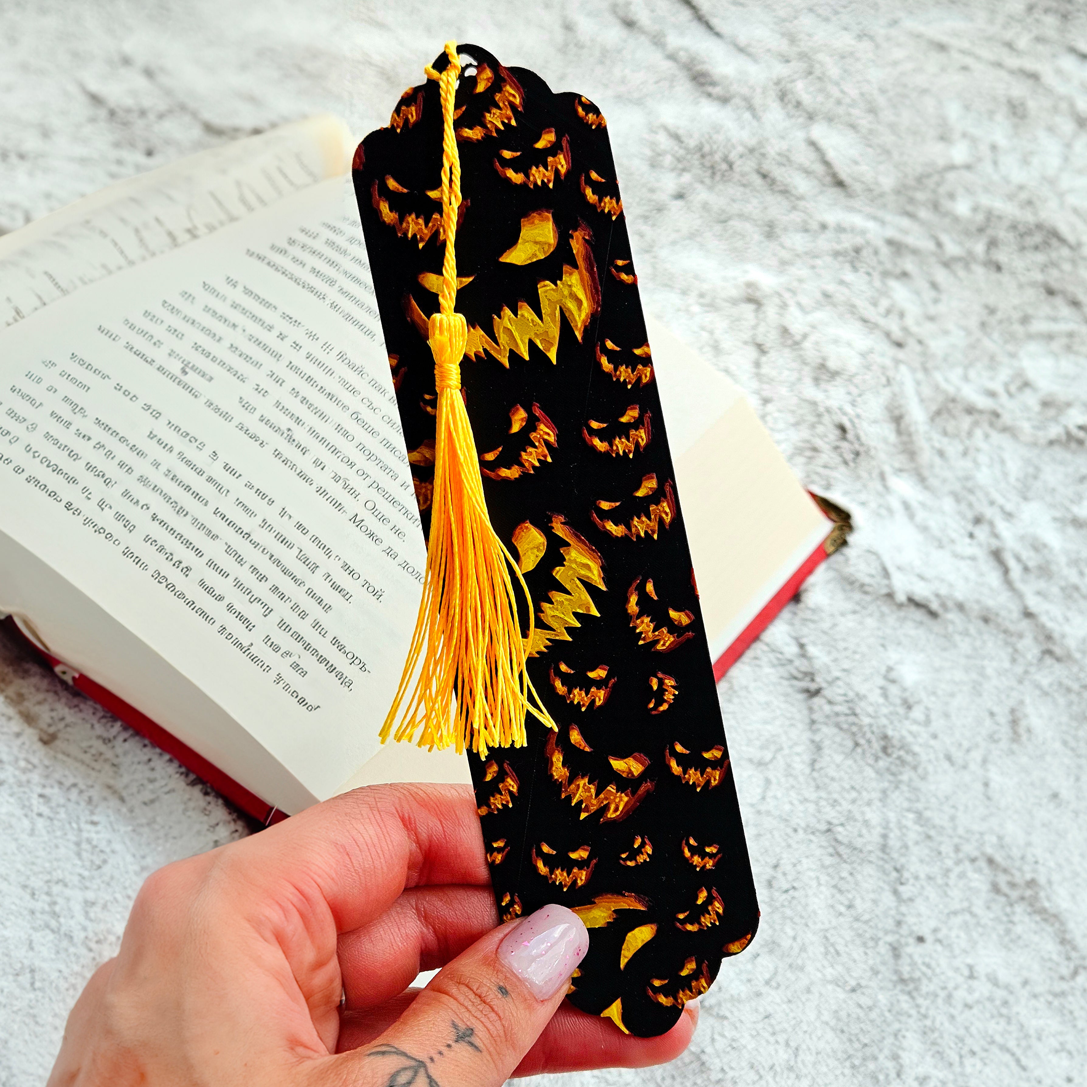 Black bookmark with yellow tassel held over an open book on a textured surface
