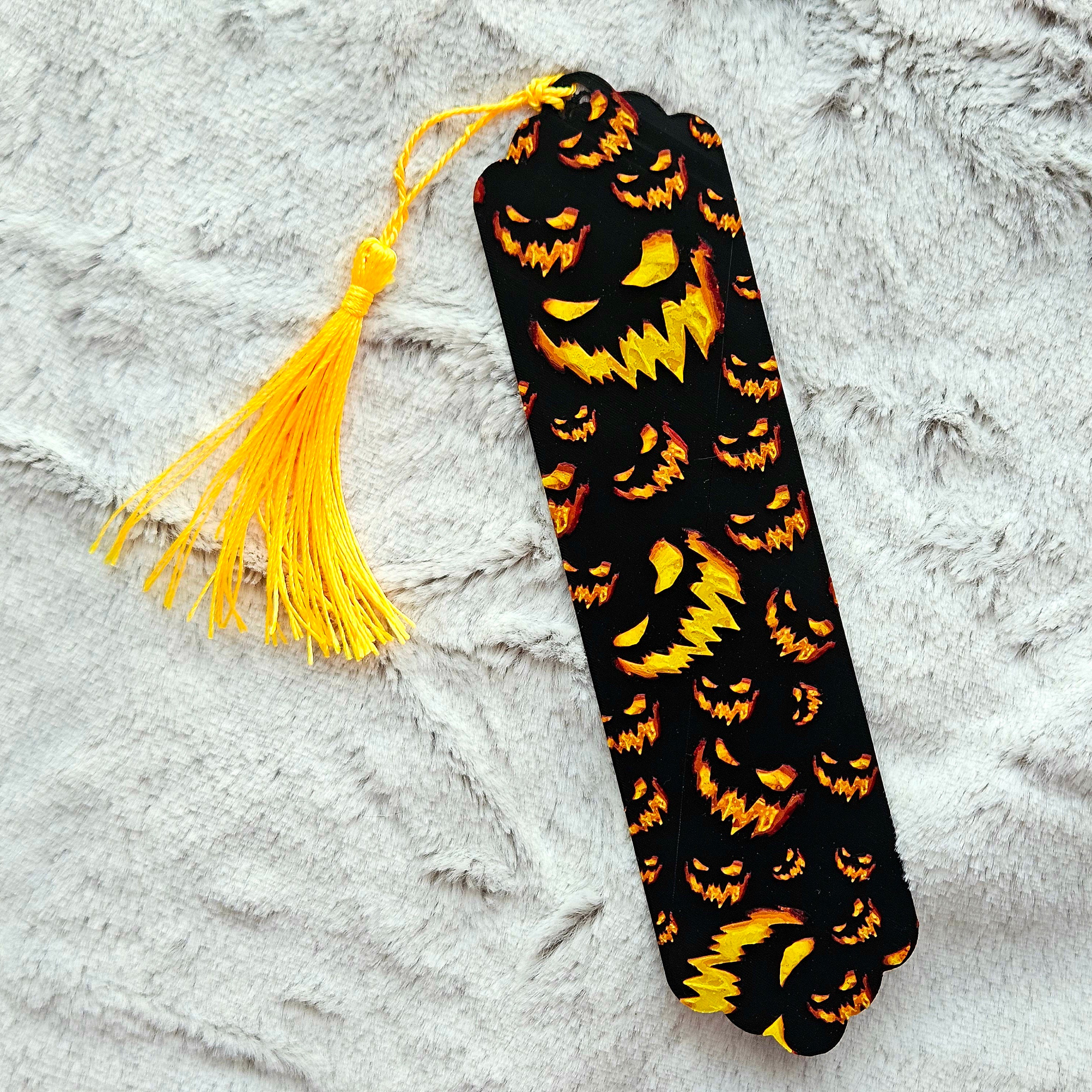 Black bookmark with orange pumpkin pattern and yellow tassel on a textured gray surface