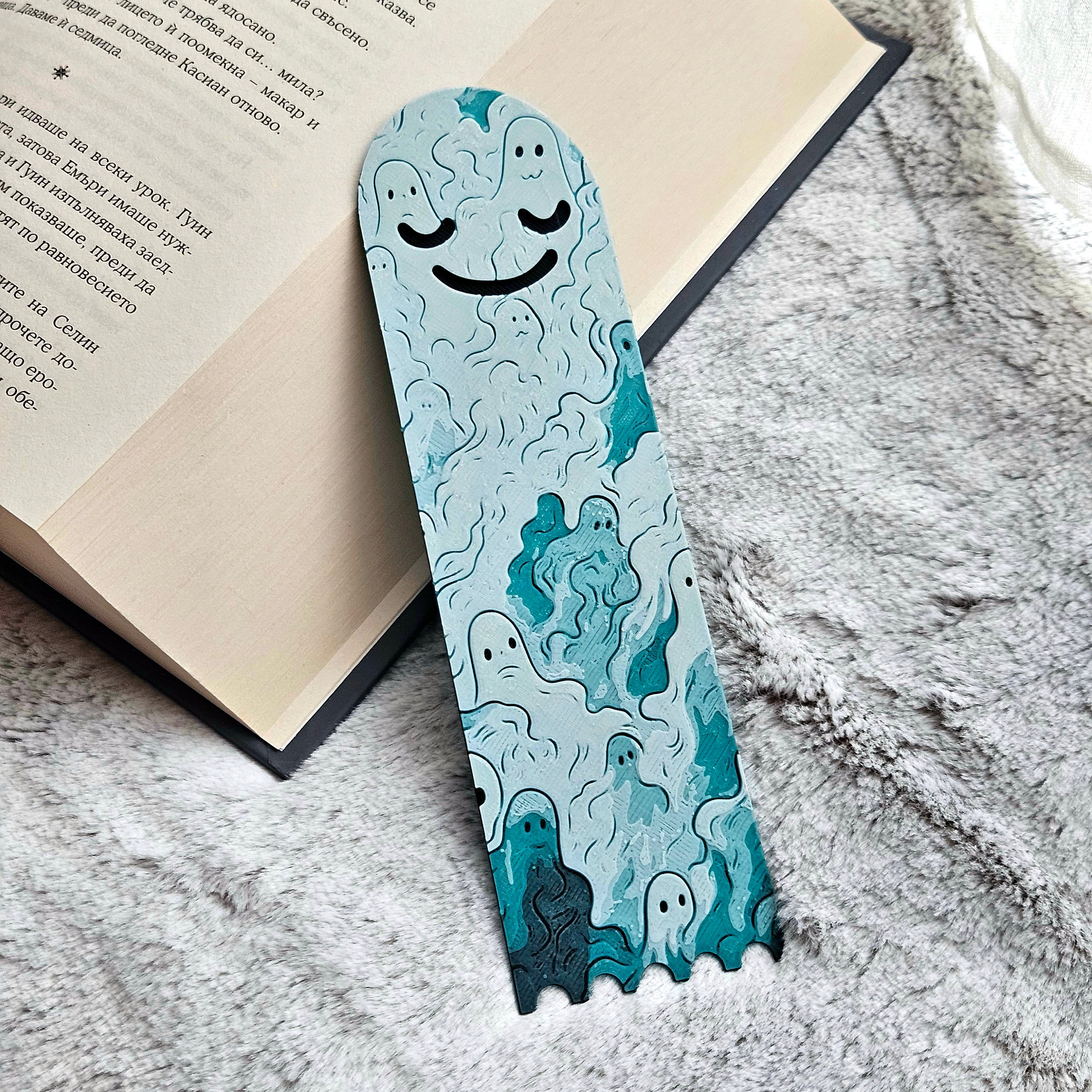 Bookmark with ghost design on a textured surface next to an open book