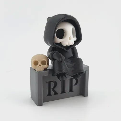 The Grave Sitter grim reaper sitting on a grey RIP headstone beside a skull