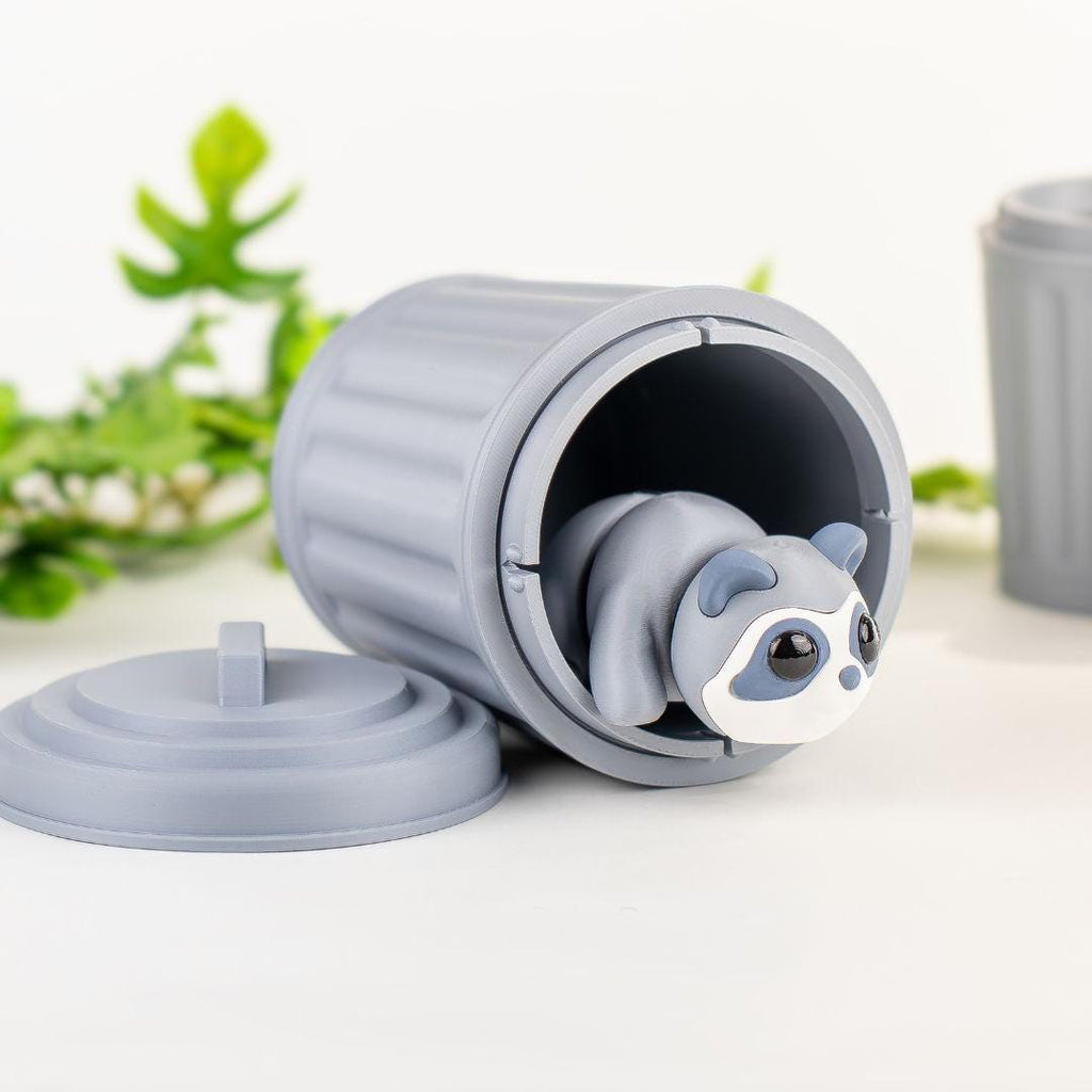 Articulated raccoon peeking out of a tipped-over mini dustbin