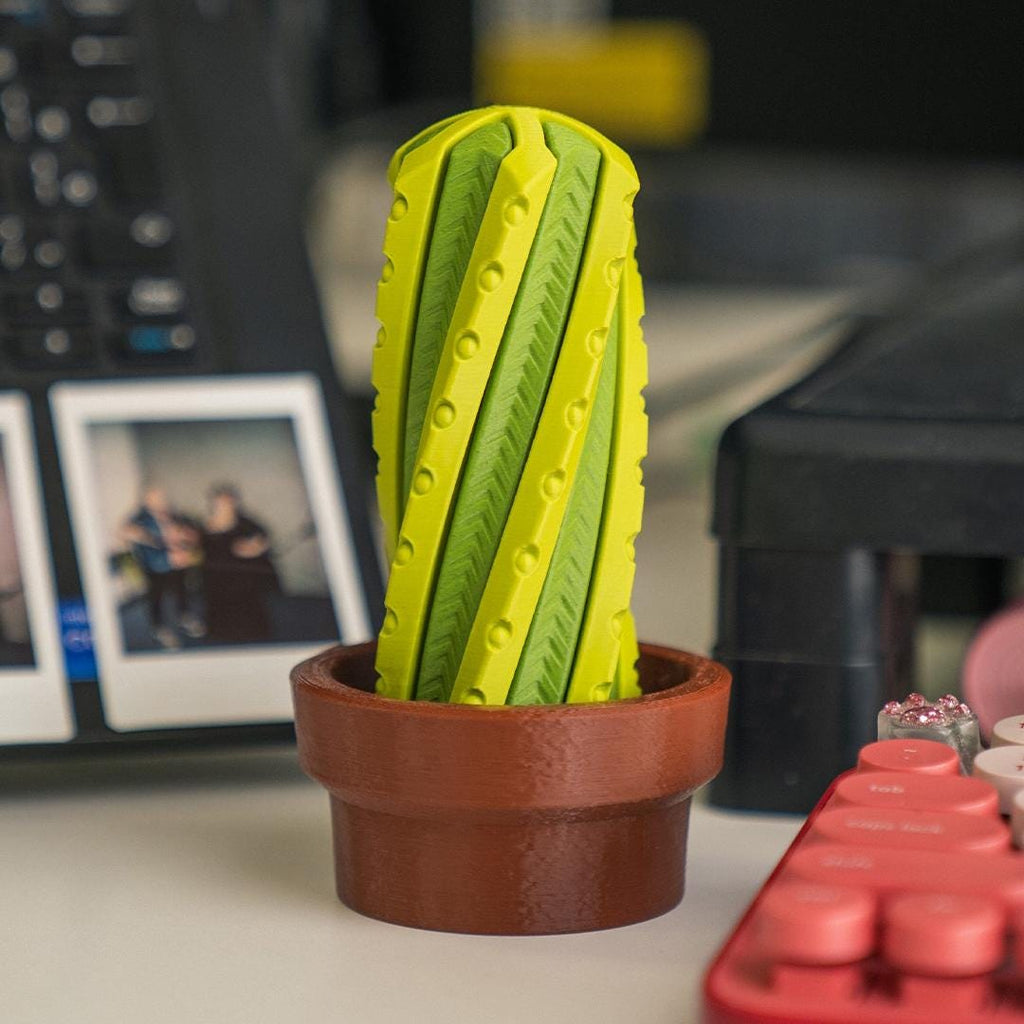 Green cactus-shaped object in a brown pot on a desk with a blurred background