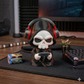 Gamer Grim Reaper figure in red headphones on a gaming desk beside a keyboard and game boxes