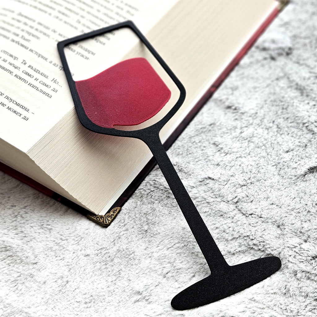 Black wine glass bookmark with red wine lying on an open book