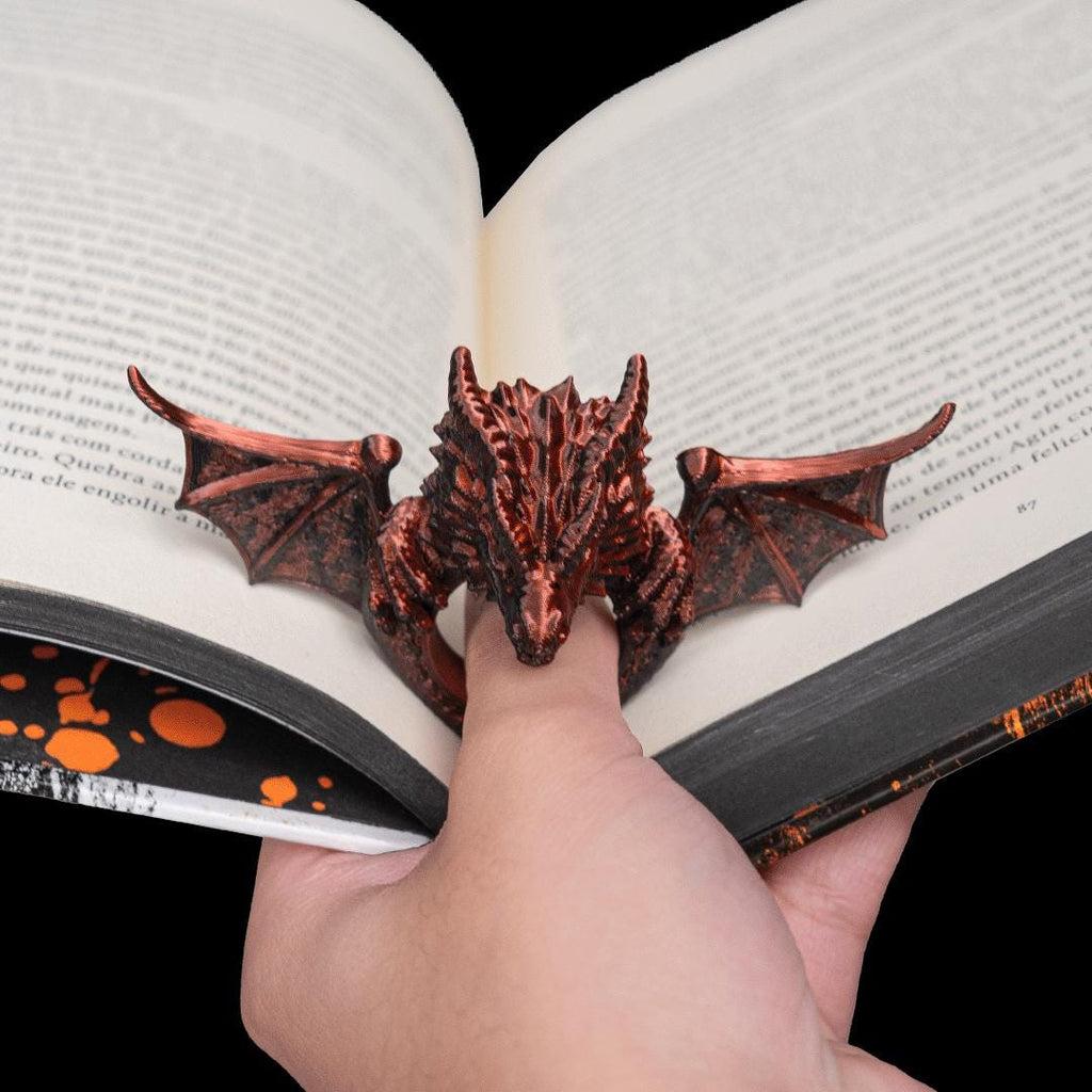 Copper dragon thumb page holder holding an open book flat, on a reader's thumb