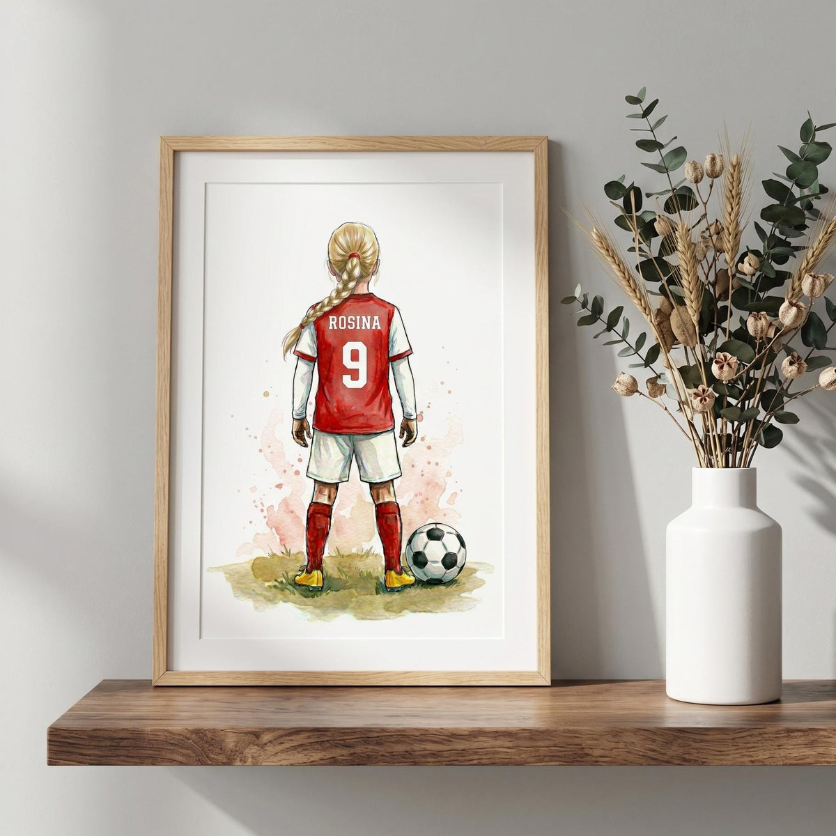 Personalised football print: a girl with a blonde plait in a red and white kit, ROSINA 9 on her shirt, in a wood frame