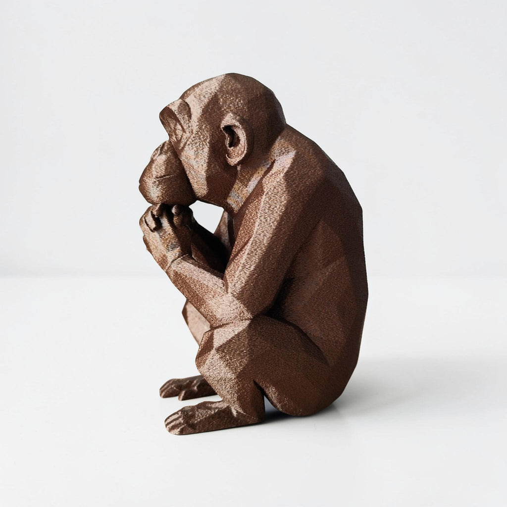 Brown monkey figurine sitting with hand on chin against a white background