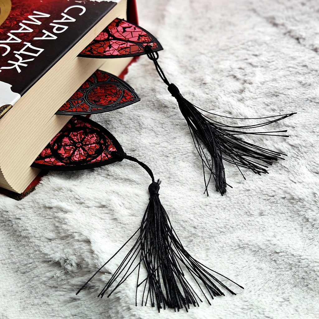 The tops of three stained glass bookmarks with tassels poking out of a red book