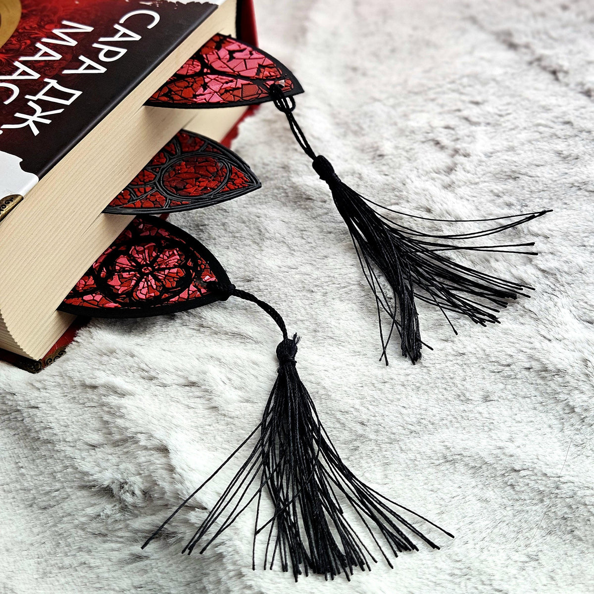 The tops of three stained glass bookmarks with tassels poking out of a red book