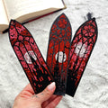 A hand holding the three gothic stained glass bookmarks