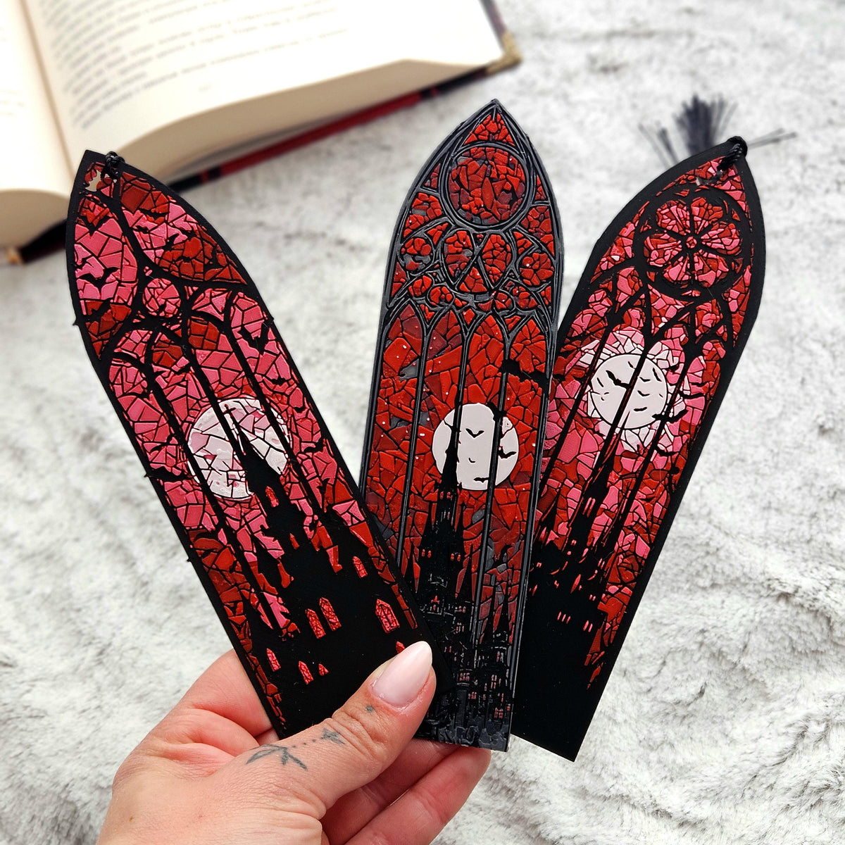 A hand holding the three gothic stained glass bookmarks