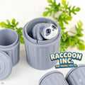 Grey articulated raccoon peeking out of a mini dustbin