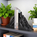 Black mountain-shaped bookends on a shelf with books and plants