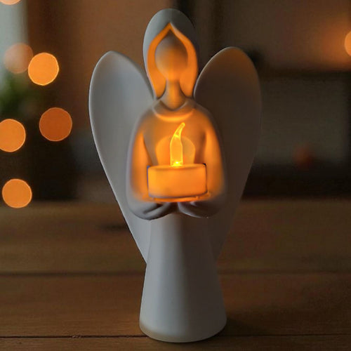 White angel figurine holding a lit candle against a warm, blurred background