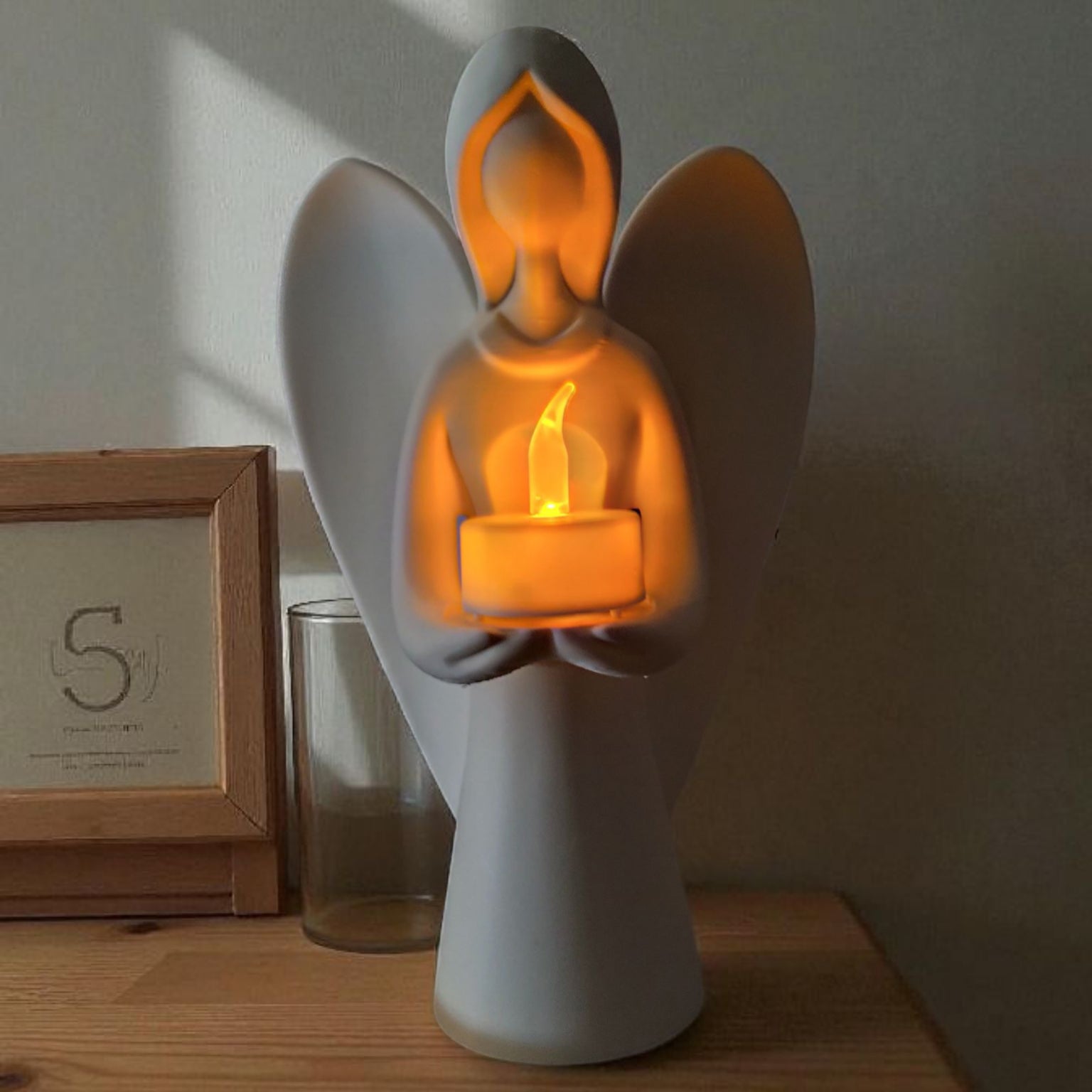 White angel figurine holding a lit candle on a wooden surface with a blurred background