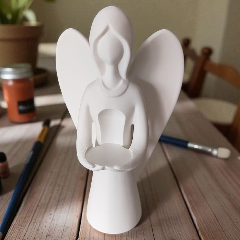 White angel figurine on a wooden surface with art supplies in the background