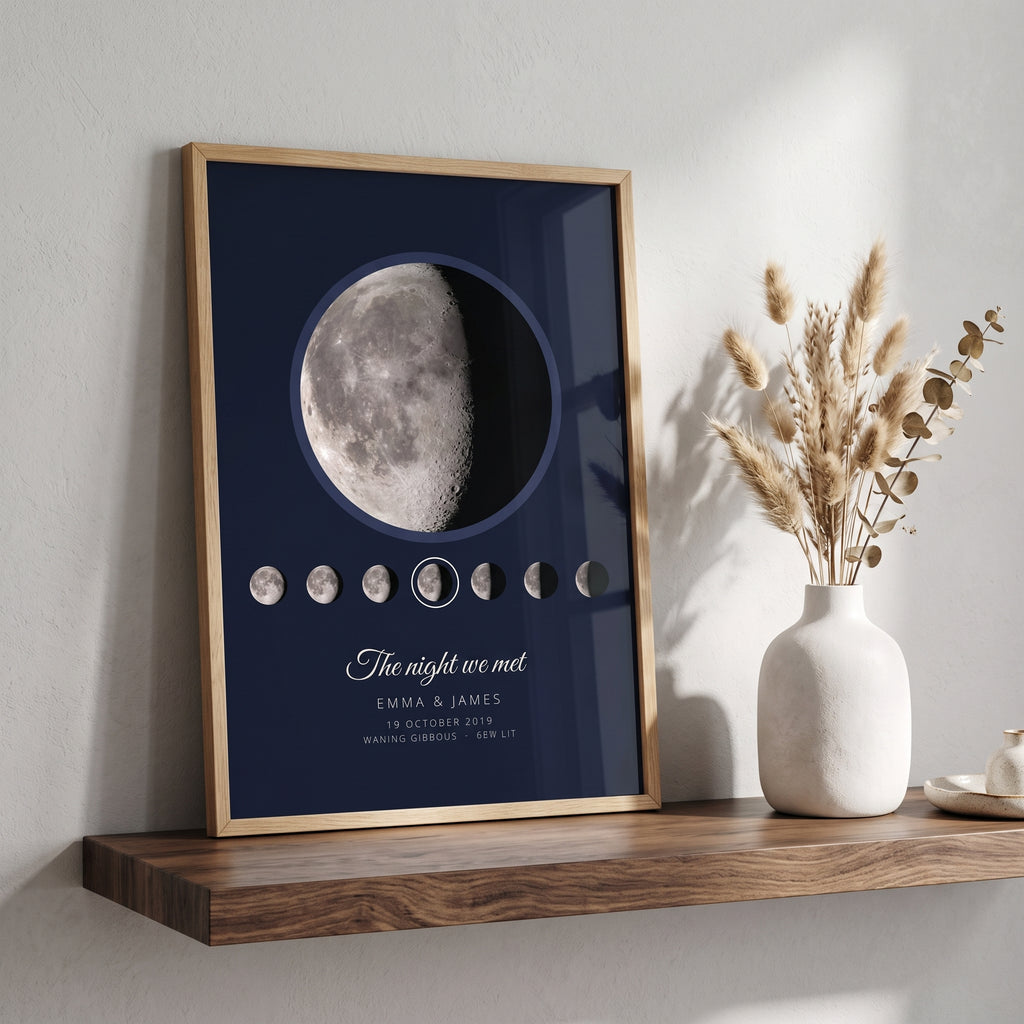 Personalised moon phase print in an oak frame on a wooden shelf: the real Moon on a navy night sky, The night we met, Emma & James, beside a vase of dried grasses