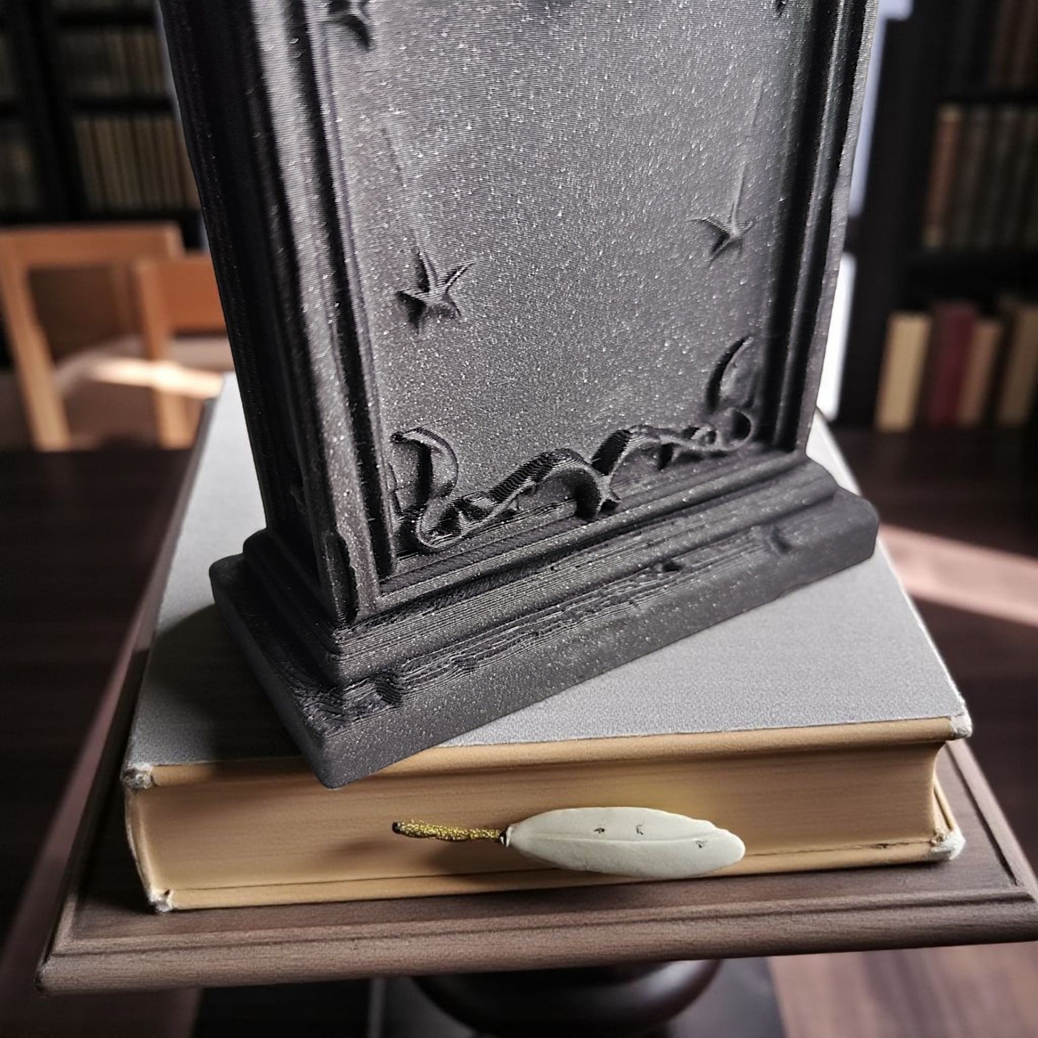 Decorative black box on top of a book with a quill pen on a wooden surface.