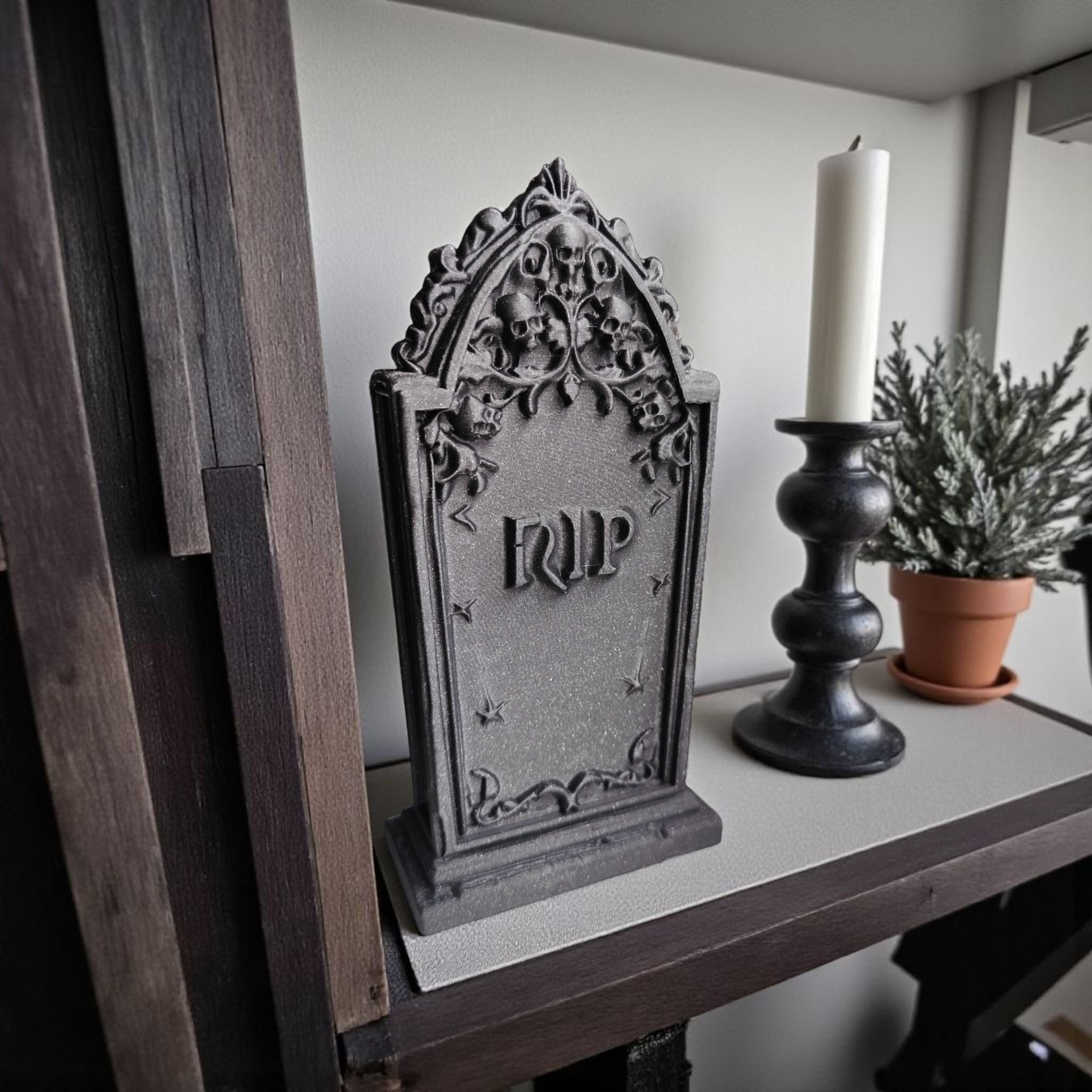 Decorative gravestone with 'RIP' on a shelf with a candle and plant