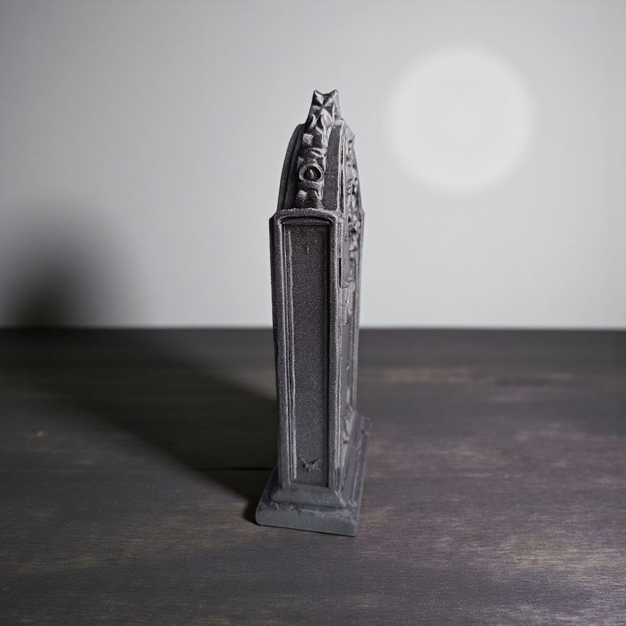 Decorative black tower-like object on a dark surface with a neutral background