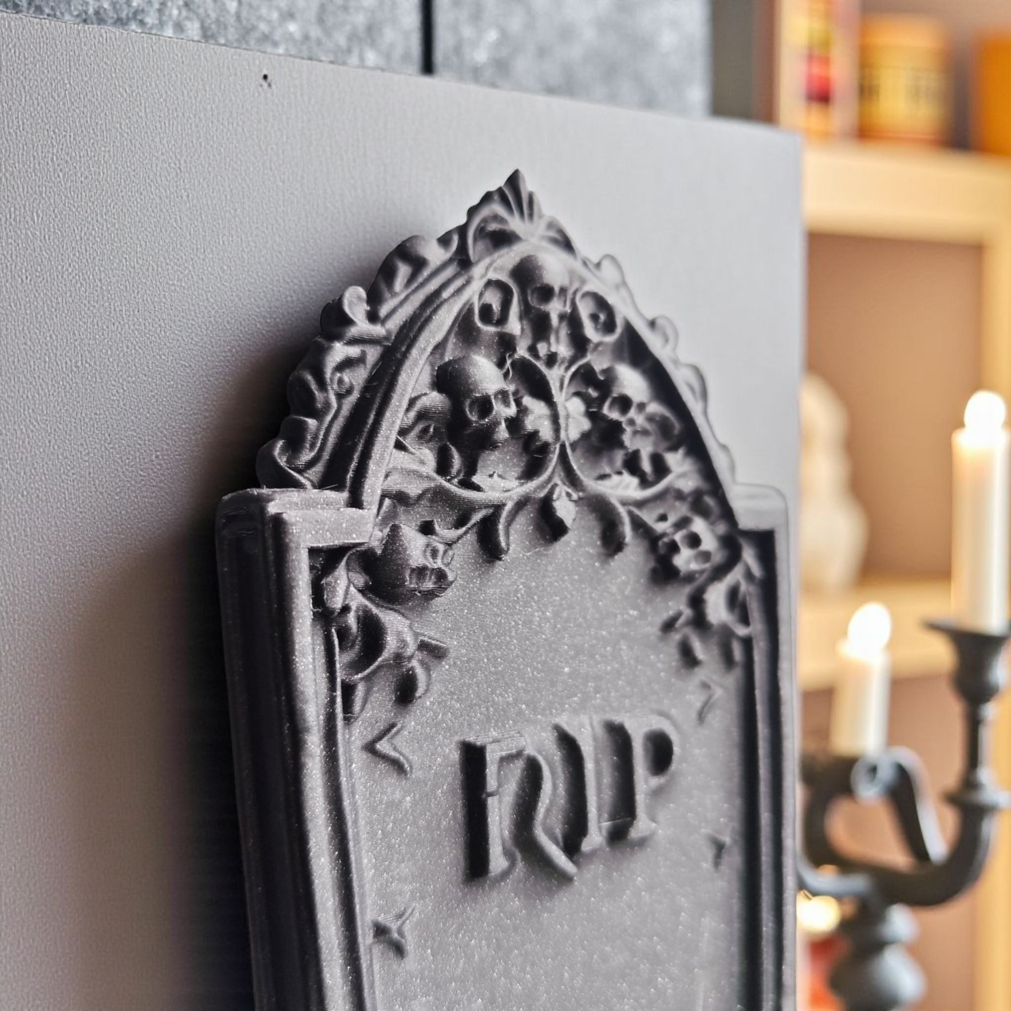 Decorative gravestone with 'RIP' on a white surface, blurred background with candles.