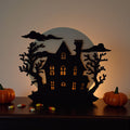 Halloween-themed decorative cutout with a haunted house silhouette, pumpkins, and candy on a wooden surface.