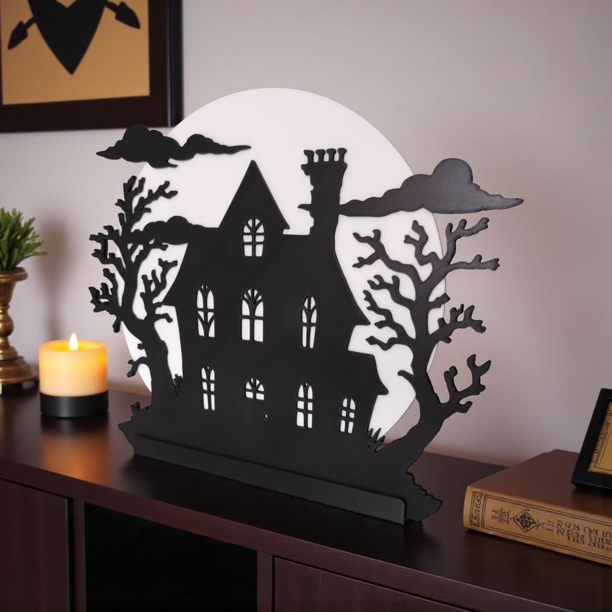 Decorative Halloween house silhouette with candle and books on a table.