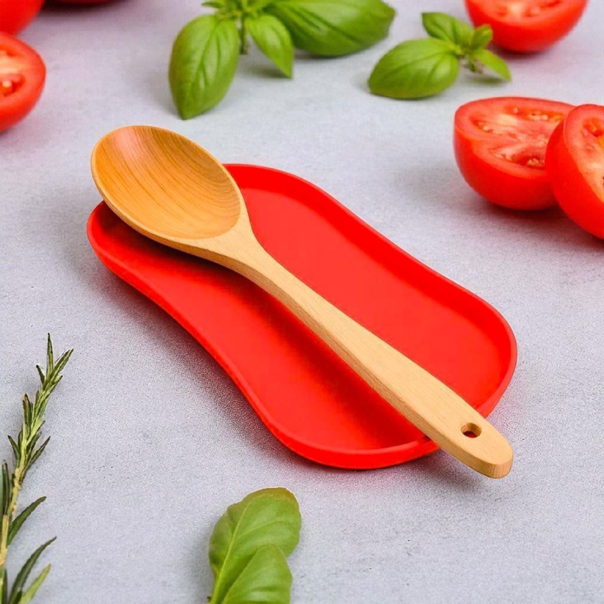 Wooden spoon on a red tray with tomatoes and basil leaves on a light gray background