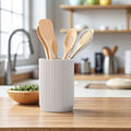 White utensil holder with wooden spoons and a whisk on a kitchen counter.