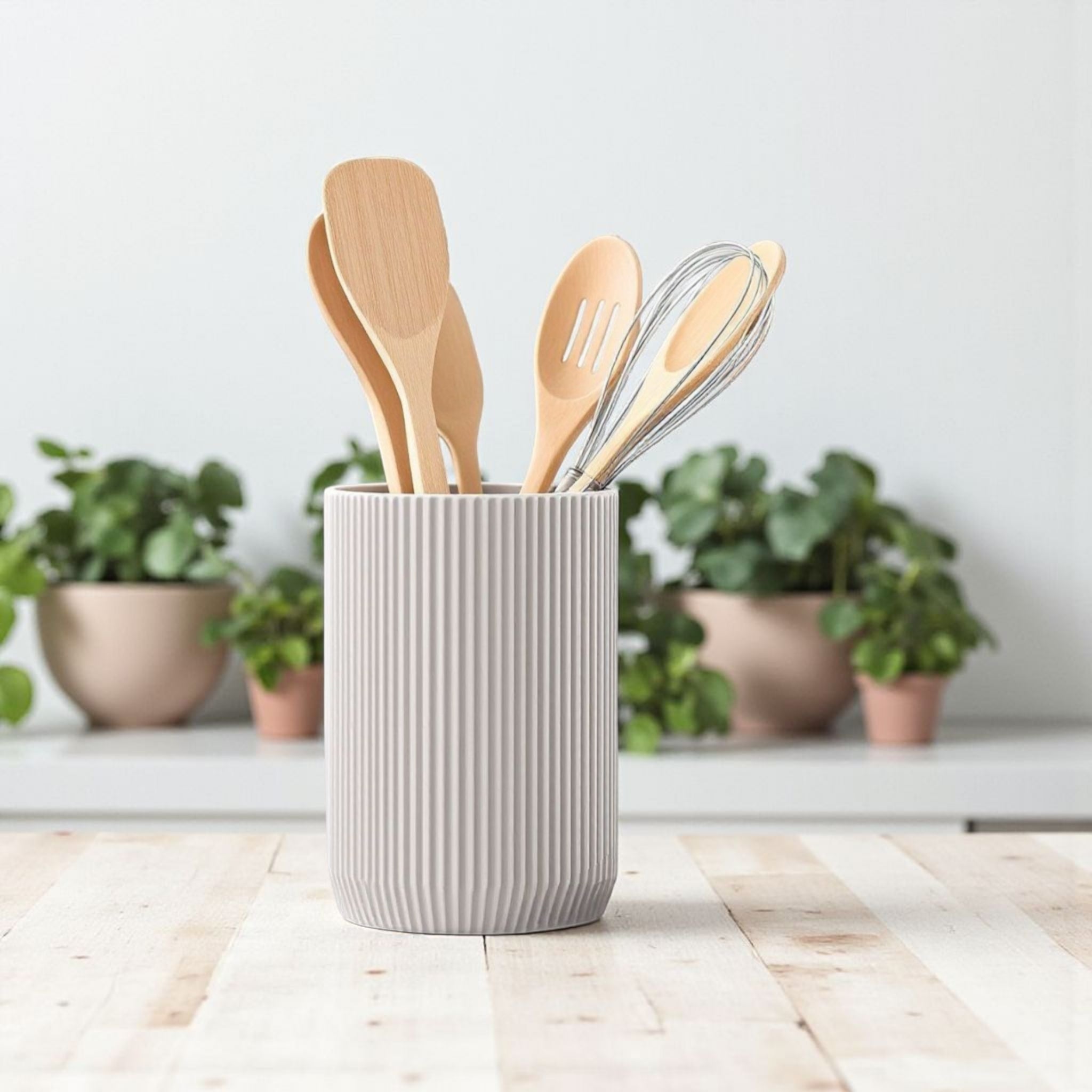 Set of wooden utensils in a textured gray holder on a light wooden surface with plants in the background.