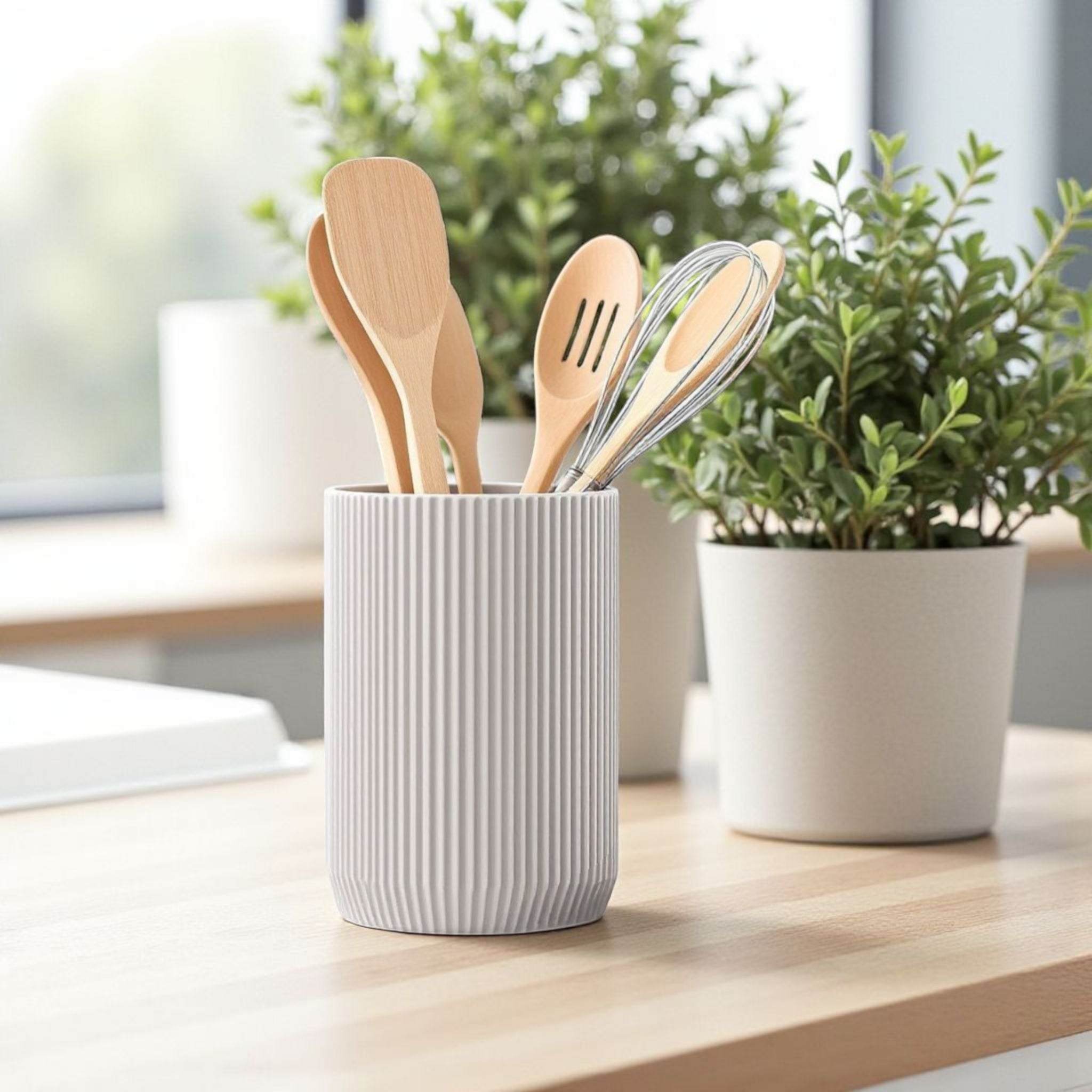 White textured cup with wooden utensils on a wooden surface with a plant in the background