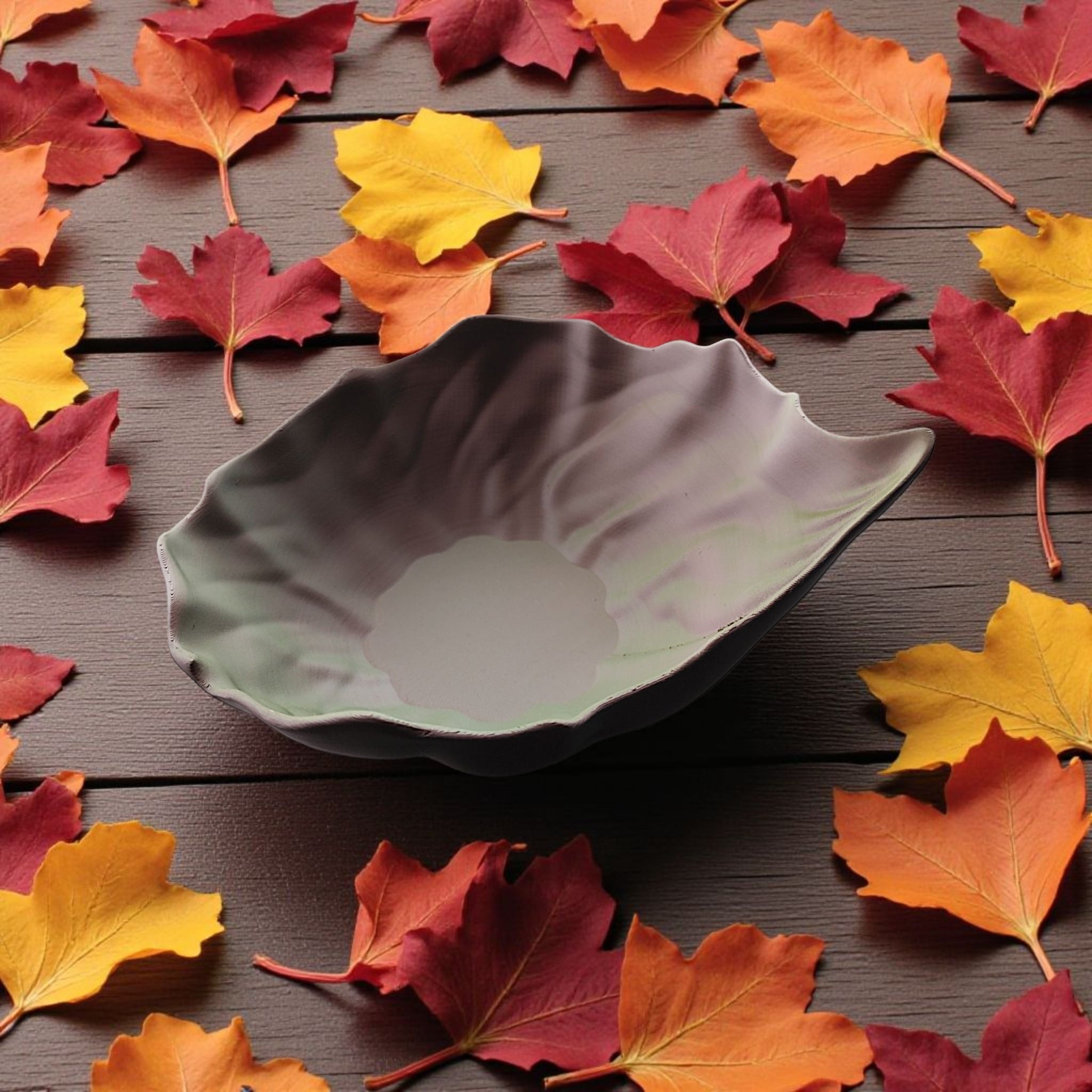 Decorative leaf-shaped bowl on a wooden surface with autumn leaves